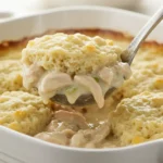 Spoon scooping creamy chicken and dumpling casserole from baking dish